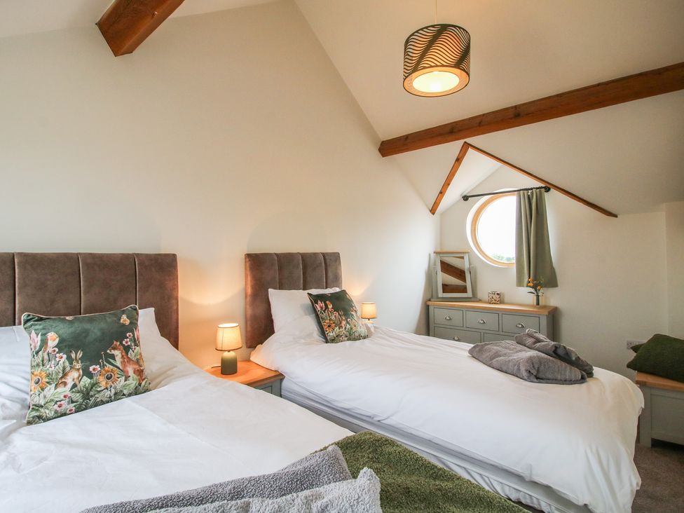 A bedroom with two beds and a circular window at Ash Barn Northwood near Wem