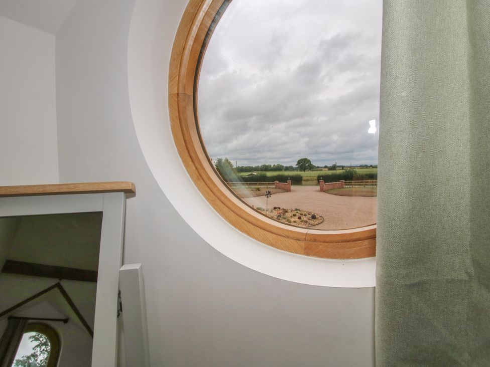 A round window with a view of a driveway and landscape at Ash Barn Northwood near Wem