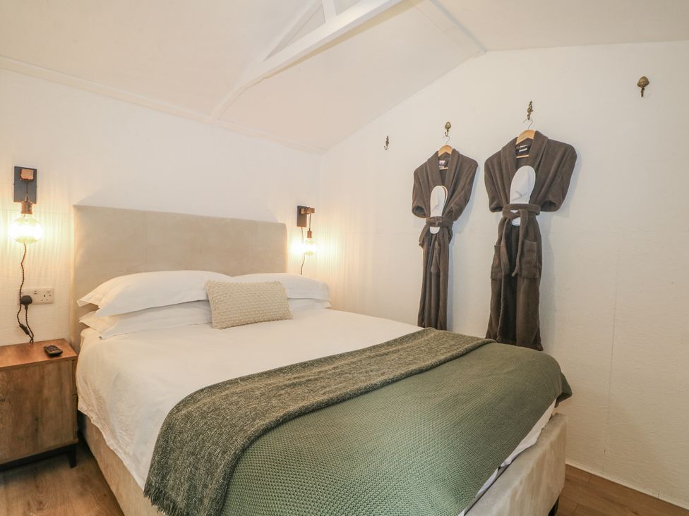 A bedroom with a bed and robes hanging on the wall at Charltons Hollow Cabin in Haywards Heath