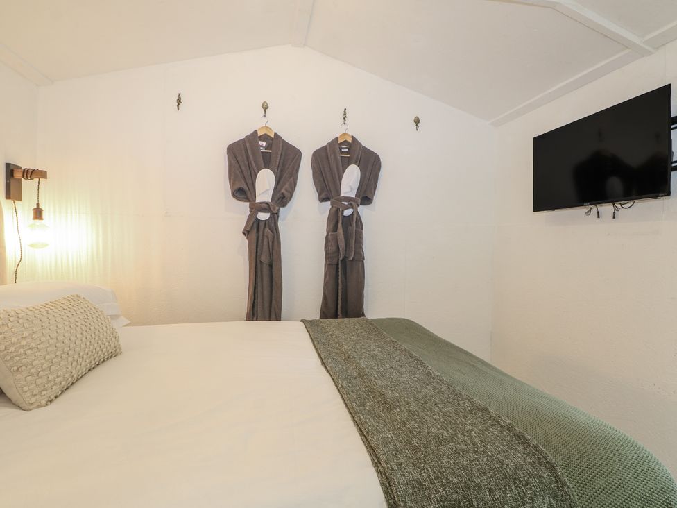 A bedroom with a bed and robes on the wall at Charltons Hollow Cabin Haywards Heath
