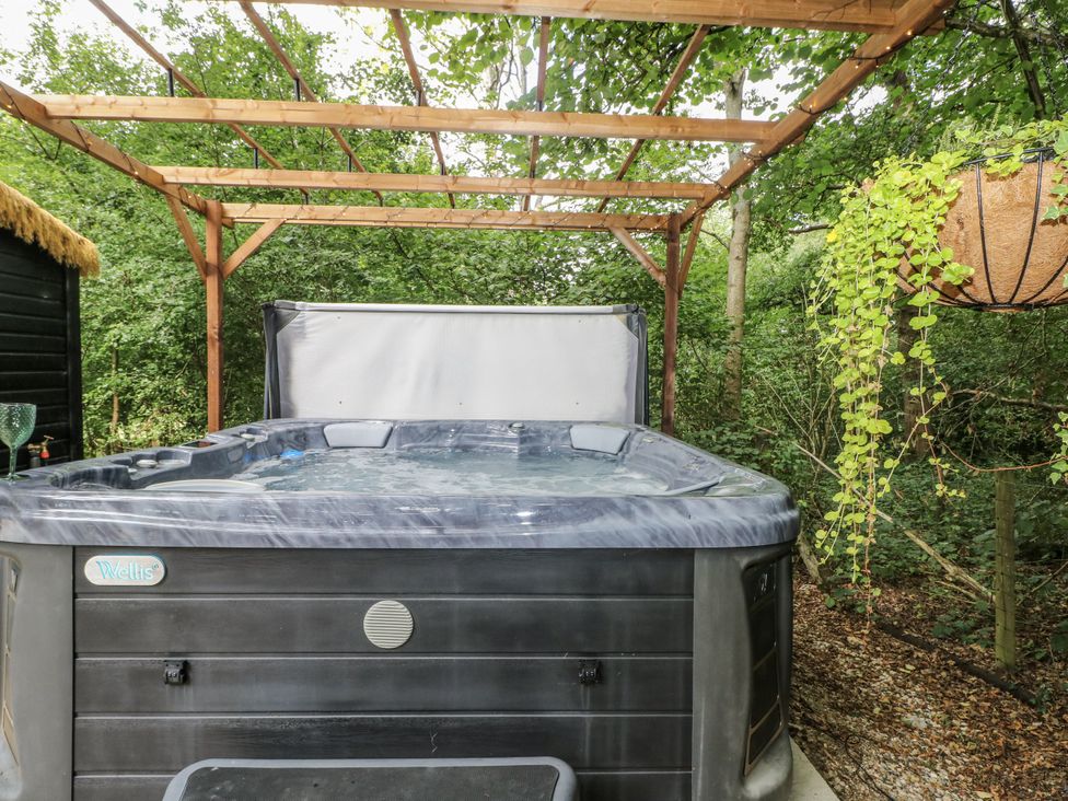 A hot tub under a wooden structure in an outdoor area at Charltons Hollow Cabin in Haywards Heath