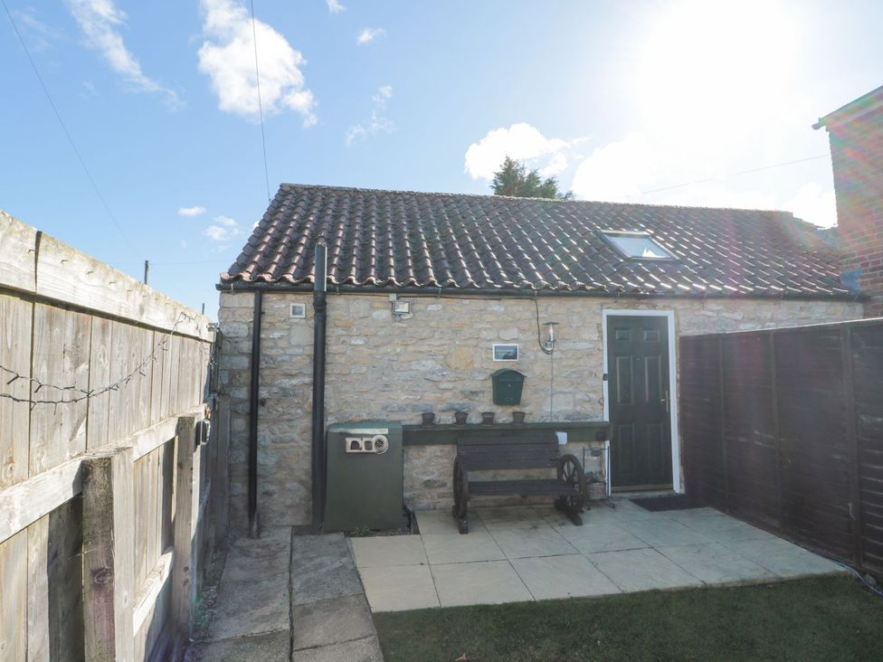 A garden area with a stone wall and a bench at Midsummer Cottage in Malton