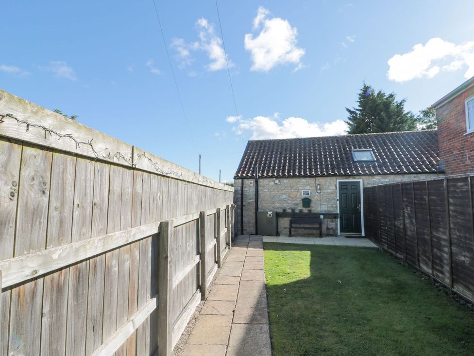A garden with a stone building and wooden fence at Midsummer Cottage Malton
