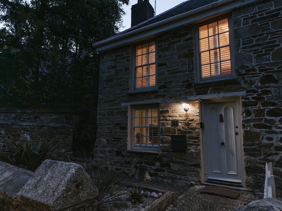 A stone house with lit windows and a door at Tamarisk Cottage in St. Agnes