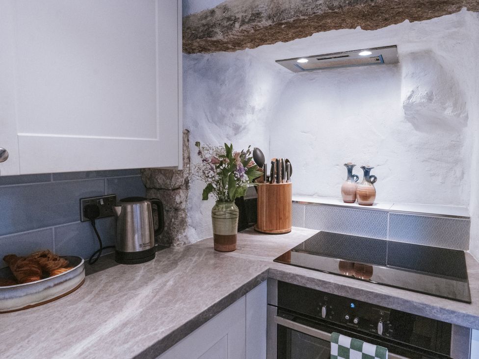 A kitchen with kettle, cooking surface, and flowers at Tamarisk Cottage in St. Agnes