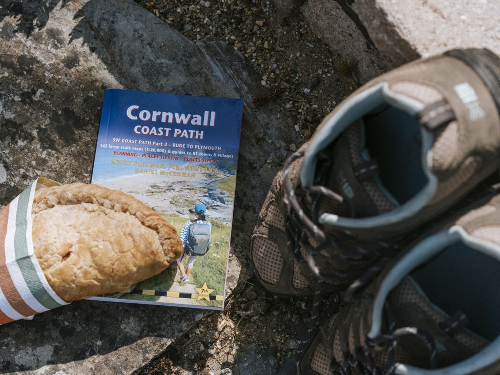 A Cornwall Coast Path guidebook with a pasty and hiking shoes outdoors at Bluck's cottage St. Agnes