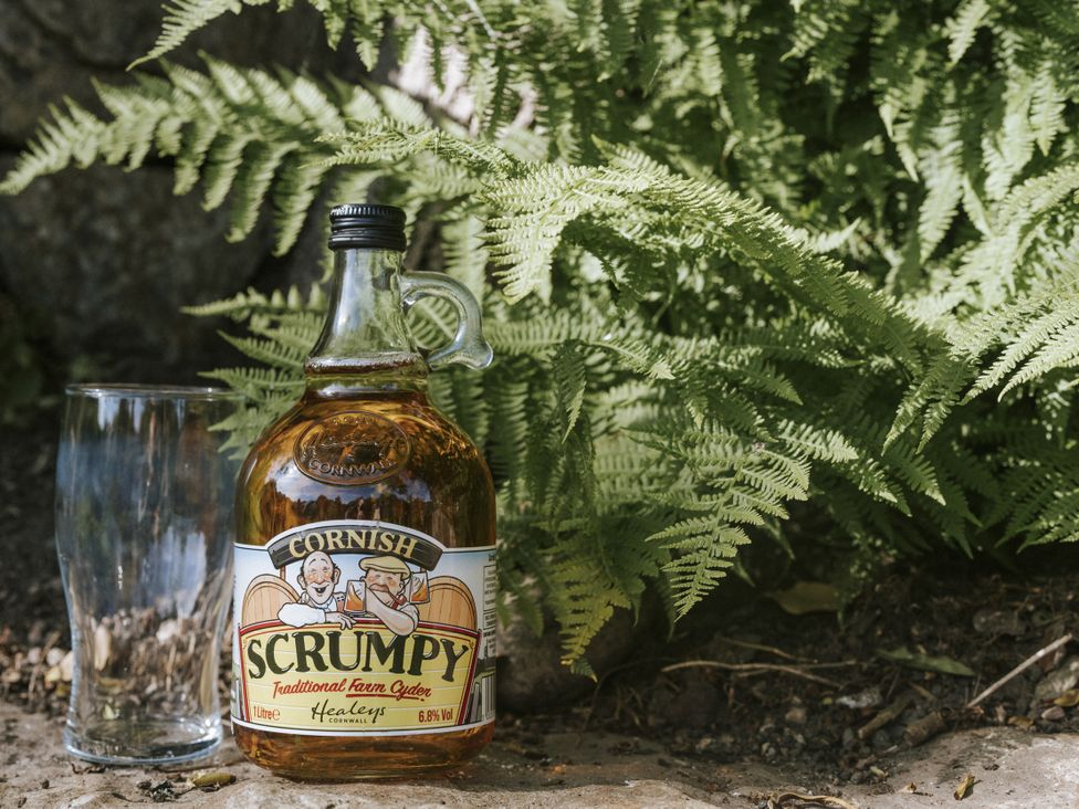 A bottle of Cornish Scrumpy cider and a glass next to ferns at Bluck's cottage St. Agnes