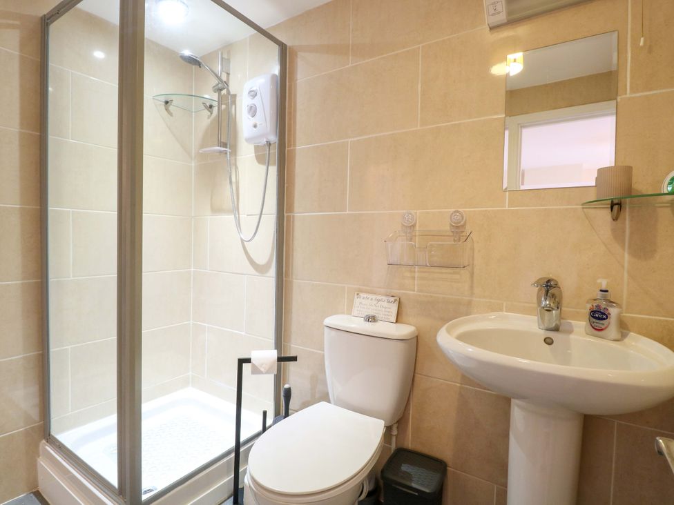 A bathroom with a shower, toilet, sink, and mirror at Honeysuckle Cottage in Swaffham