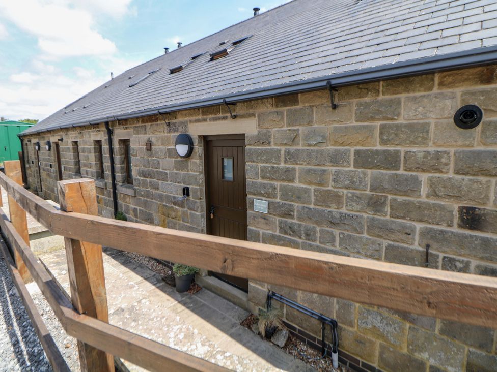 An exterior view of a stone building with a door and fence at Hollow Brook Cottage in Hope Valley