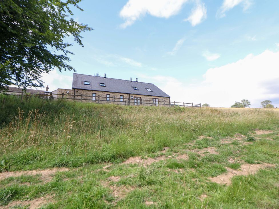 A building with a fenced area on a grassy landscape at Hollow Brook Cottage in Hope Valley