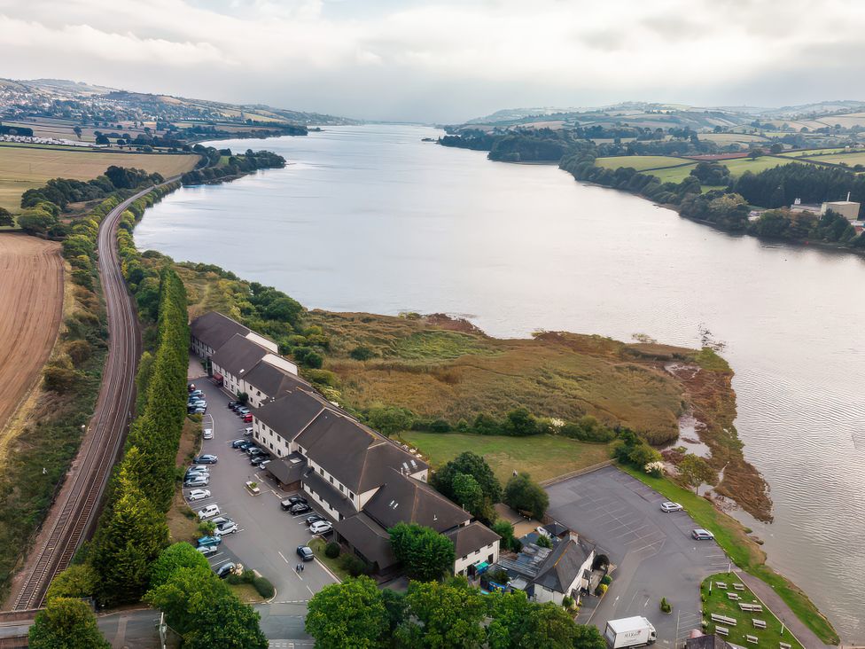 An aerial view of a river with buildings and a railway line at Guillemot in Kingsteignton