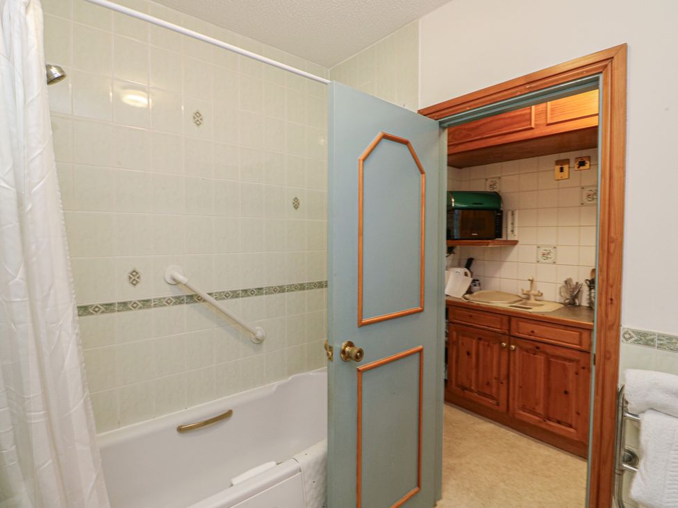 A bathroom with a bathtub and kitchenette at Sycamore in Newton Abbot