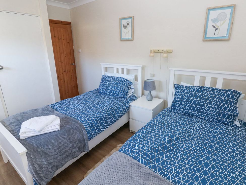 A bedroom with two beds and a bedside table at Tig Bhan in Narberth