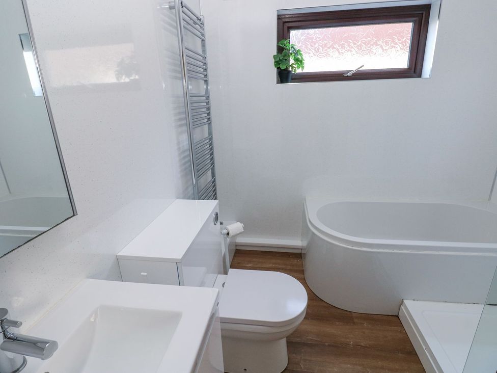 A bathroom with a bathtub, toilet, sink and mirror at Tig Bhan in Narberth