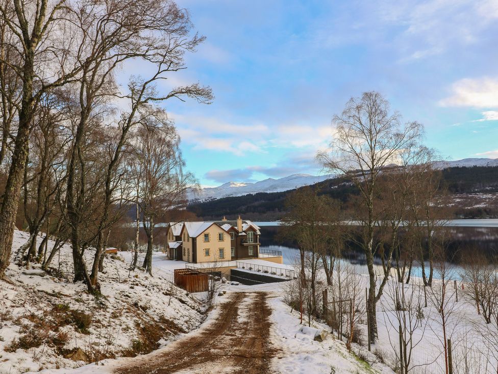 A house by a lake surrounded by trees and mountains at Schiehallion House Pitlochry