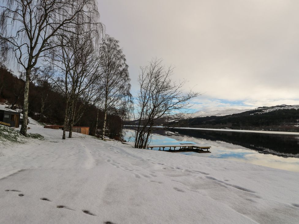 An outdoor view of a snow-covered lake with trees and a dock at Schiehallion House in Pitlochry