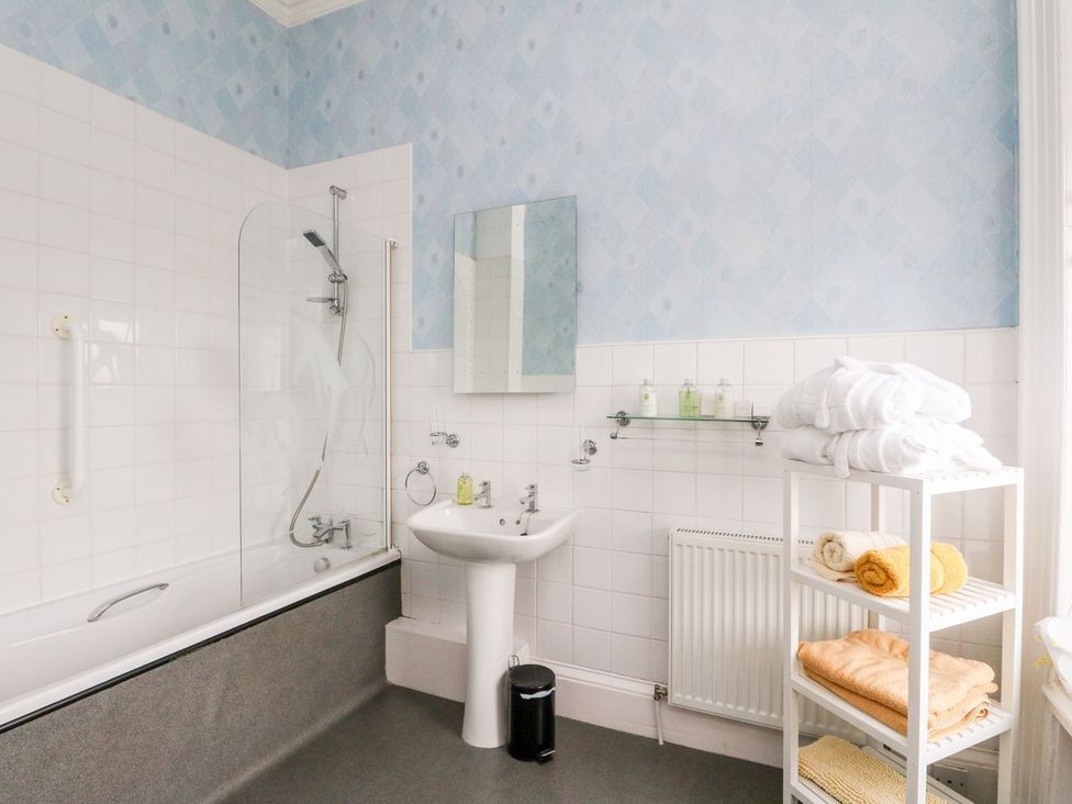 A bathroom with a bathtub, sink, and shelves of towels at Seaview Wellness Retreat in Carnoustie