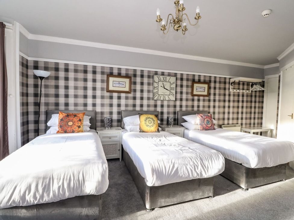 A bedroom with three beds and a clock on the wall at Seaview Wellness Retreat in Carnoustie
