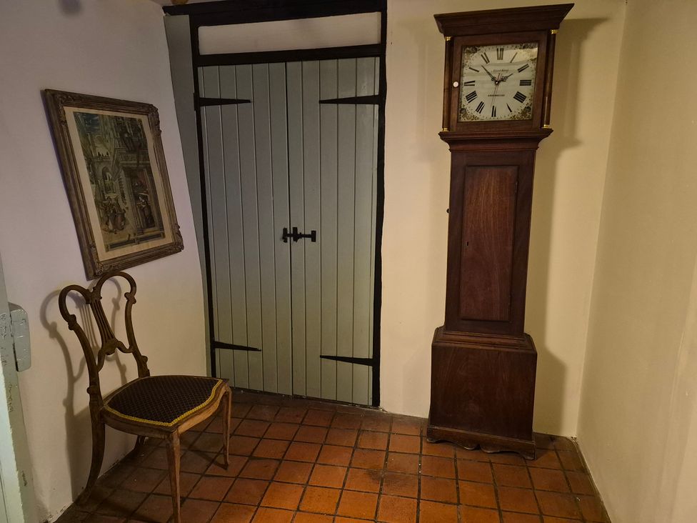 An entryway with a clock, chair, door and a painting at Clare's Cottage in Harrold