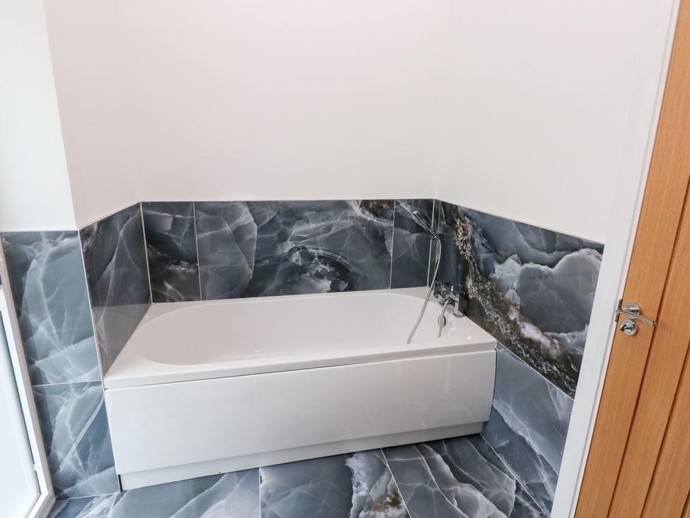 A bathroom with a bathtub and wall tiles at Cottage 1 in Laugharne