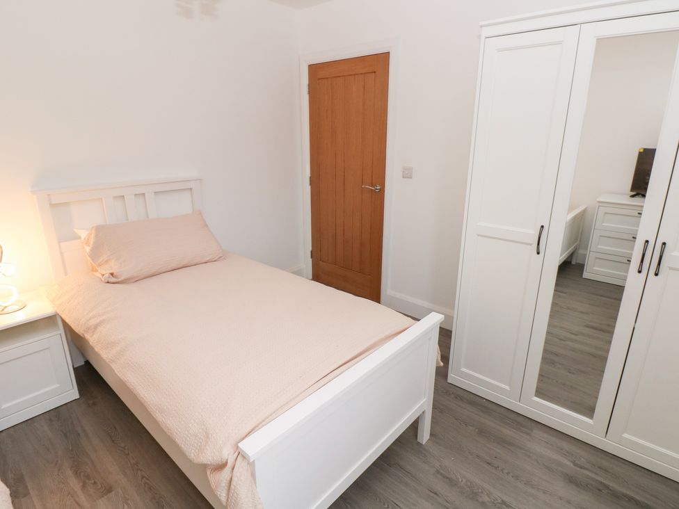 A bedroom with a bed, nightstand, lamp, and wardrobe at Cottage 1 in Laugharne