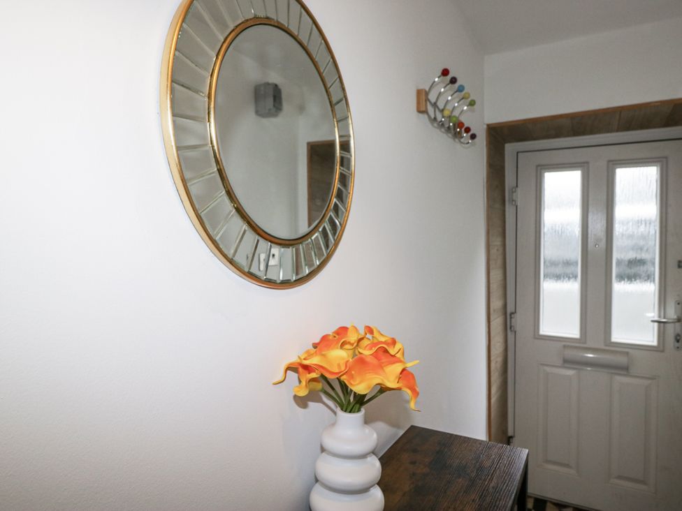 A hallway with a mirror, flowers in a vase, and a coat rack at Aspen Boutique
