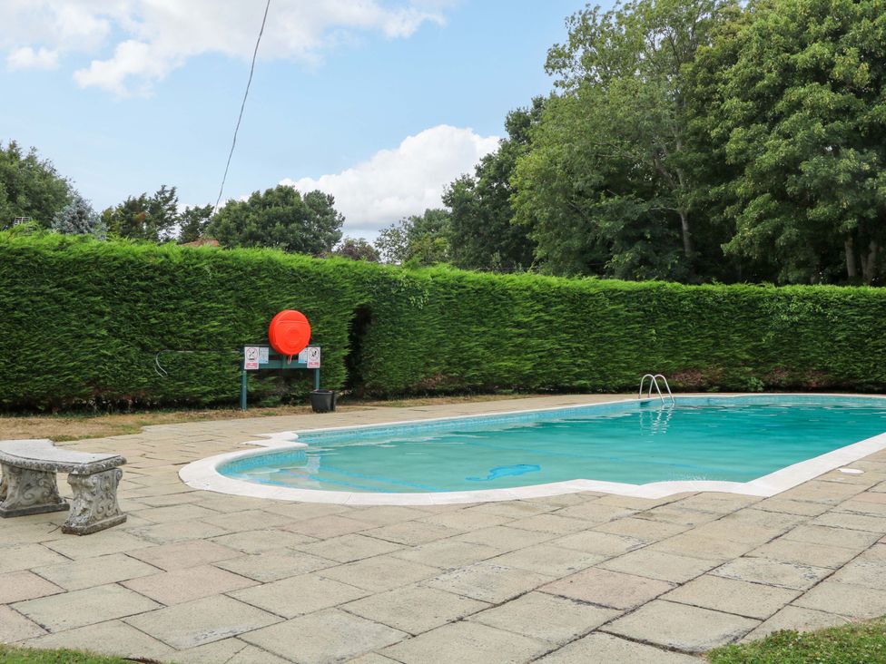 An outdoor area with a swimming pool and surrounding hedge at Daisy Cottage Pevensey
