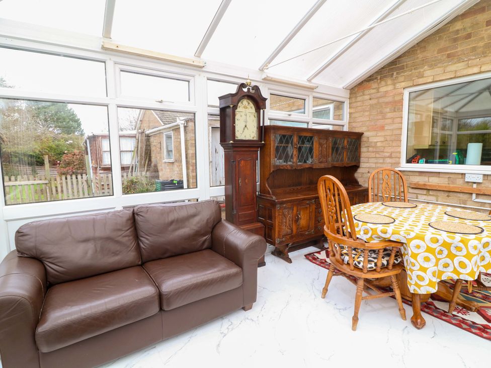A conservatory with a sofa, clock, sideboard, and dining table at 5 Overstone Drive in Wisbech