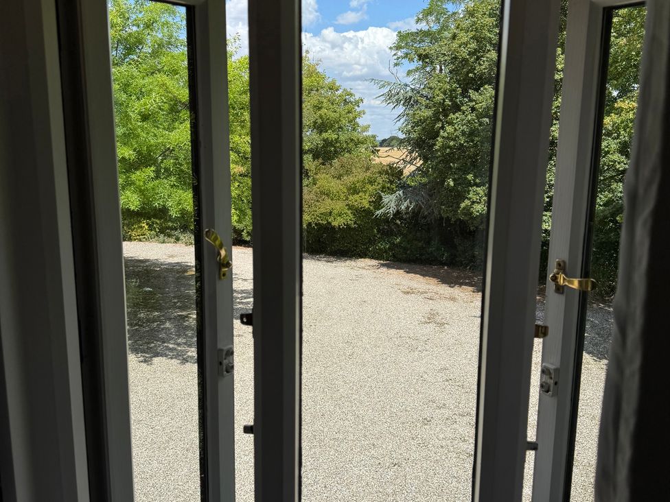 A view through a window showing trees and a gravel area at Headland Barn in Maldon