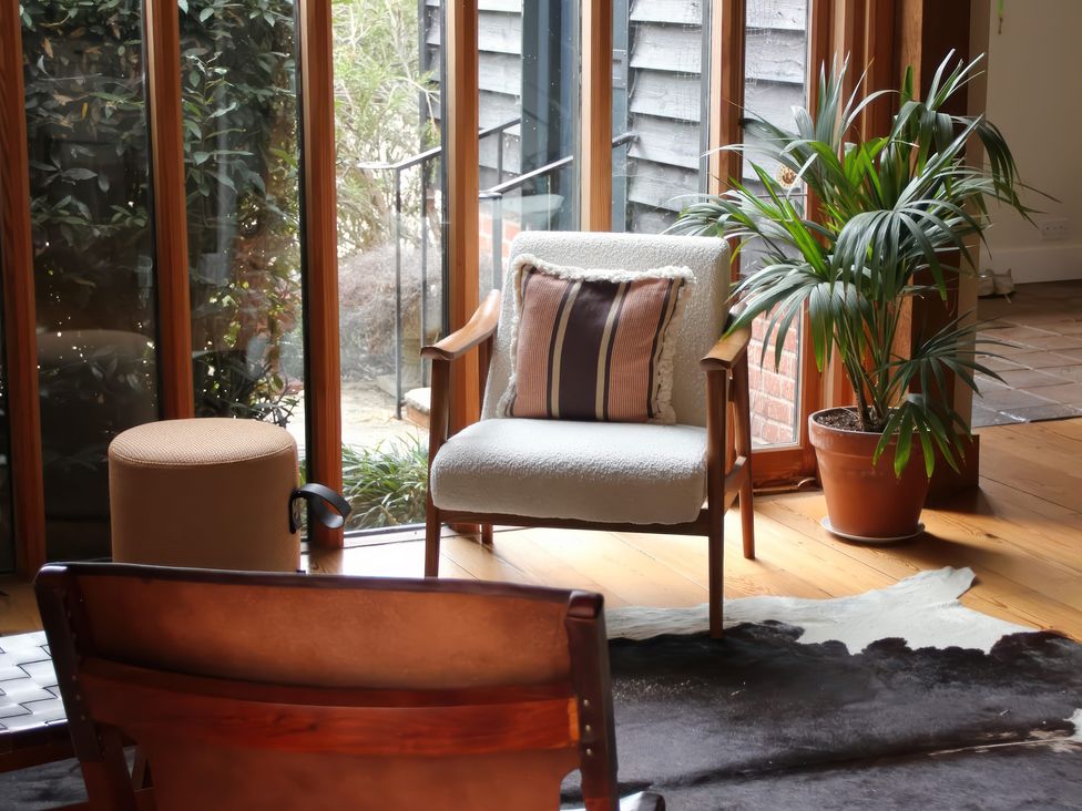 A snug area with an armchair, decorative pillow, plant, stool, and cowhide rug at Headland Barn Maldon