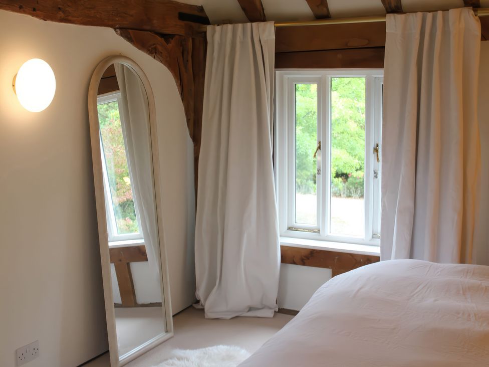 A bedroom with a mirror and window at Headland Barn in Maldon