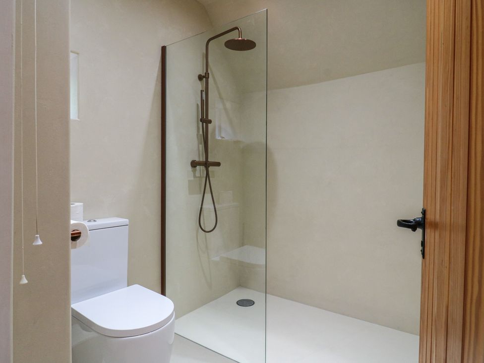 A bathroom with a toilet and a glass shower enclosure at Headland Barn in Maldon