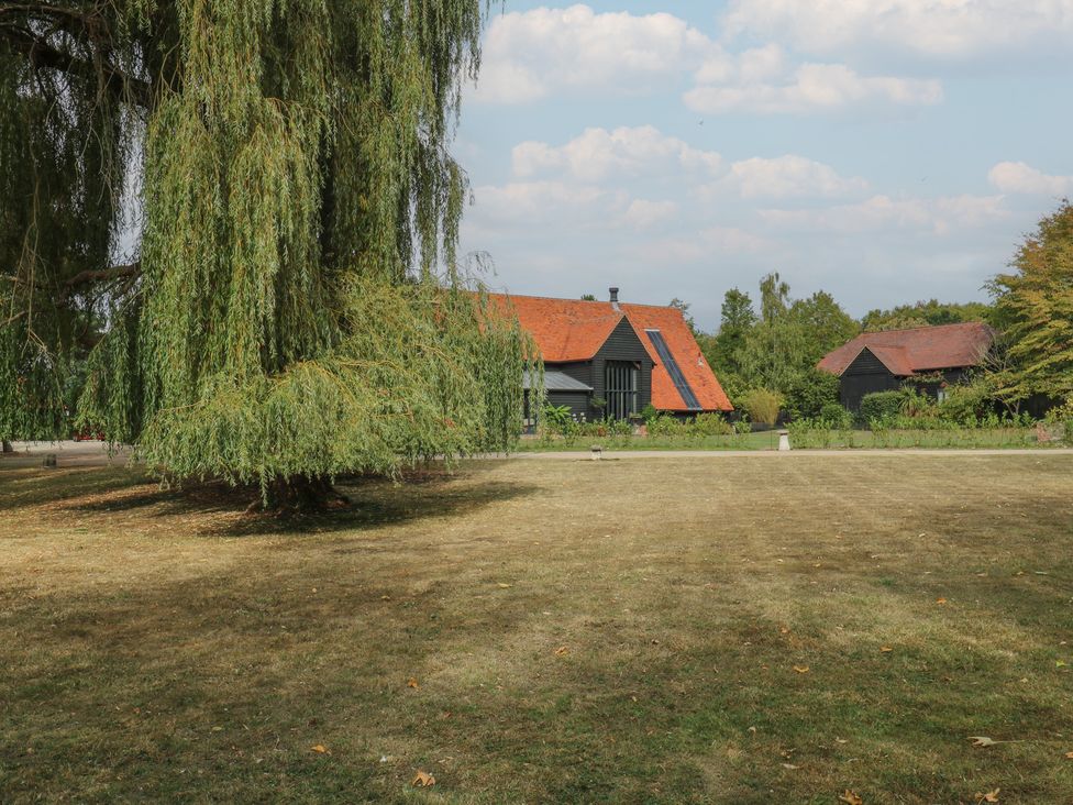 A garden with a willow tree and houses at Headland Barn in Maldon