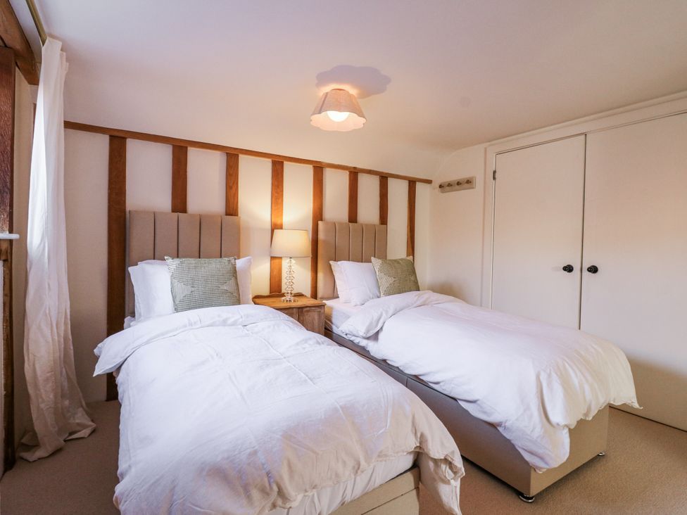 A bedroom with twin beds and a bedside lamp at Headland Barn in Maldon