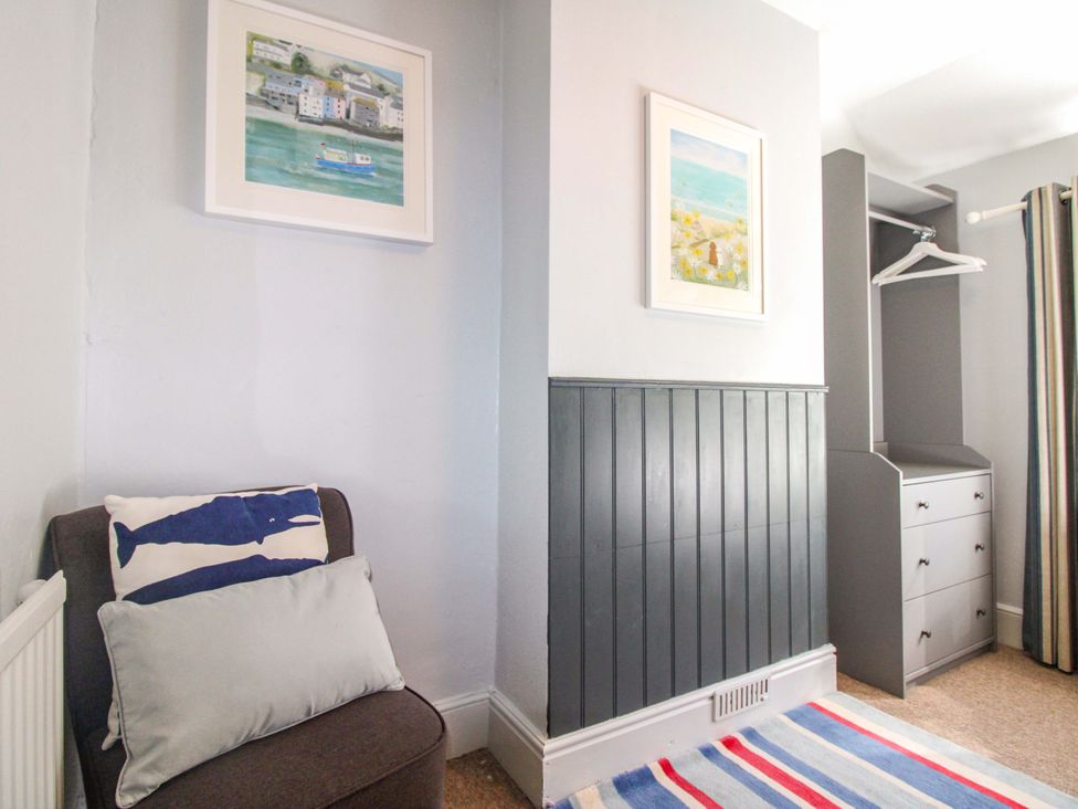 A bedroom with a chair, cushions and storage drawers at Rockside in Salcombe