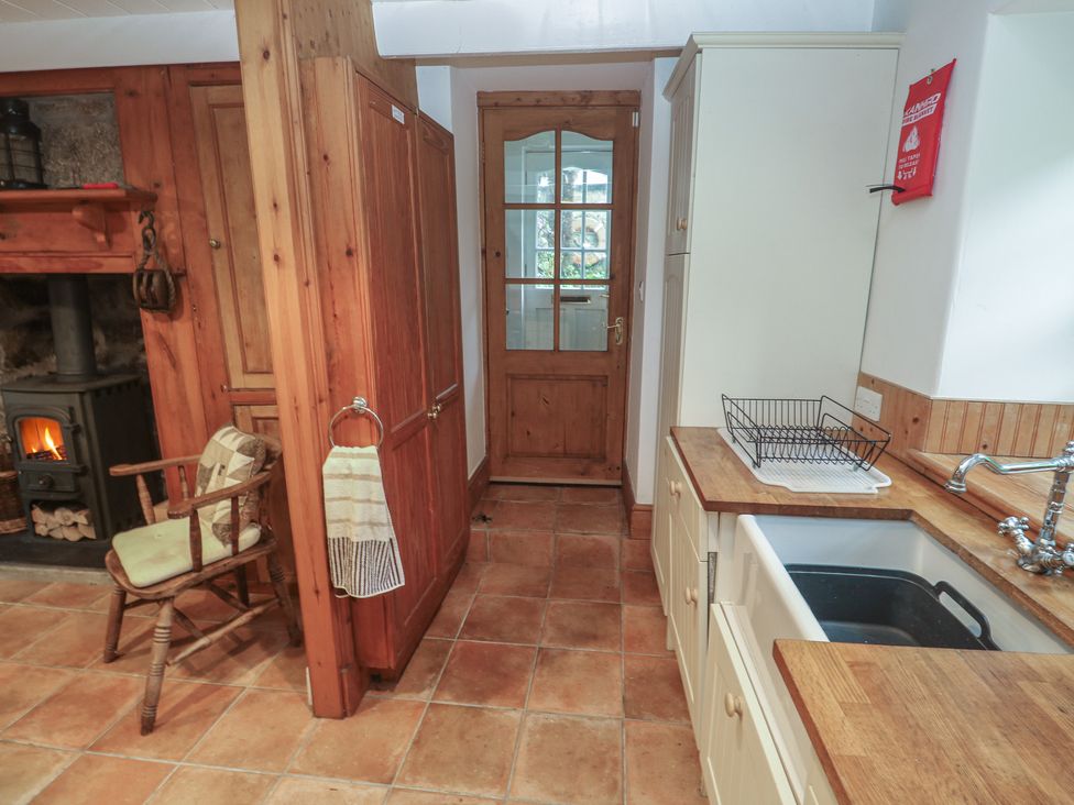 A kitchen with wooden cabinets and a fireplace at 1 Rowes Cottages in Penzance