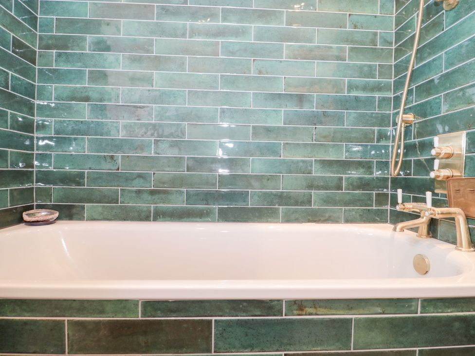 A bathtub with green tiles in a bathroom at Bohemian Beach Cottage in Bournemouth