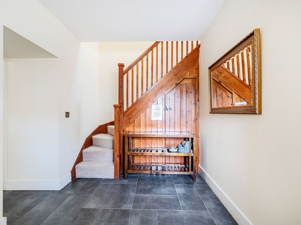 A hallway with a staircase and a storage shelf at The Dairy in Corwen