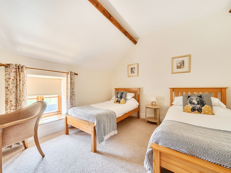 A bedroom with two single beds and an armchair at The Dairy in Corwen