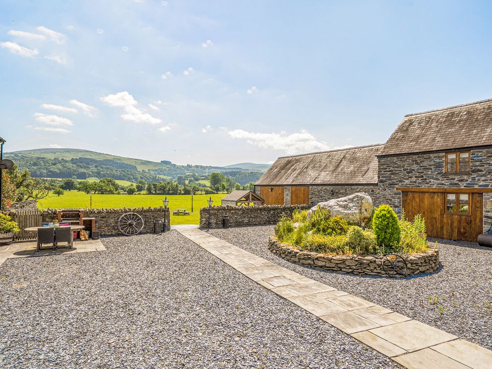 An outdoor area with gravel, stone wall, and wooden buildings at The Dairy in Corwen