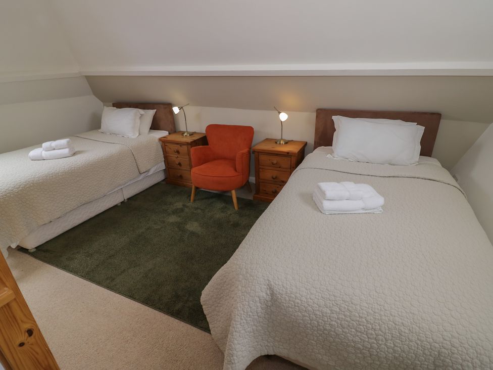 A bedroom with two beds and an orange chair at Raglan Lodge Monmouth