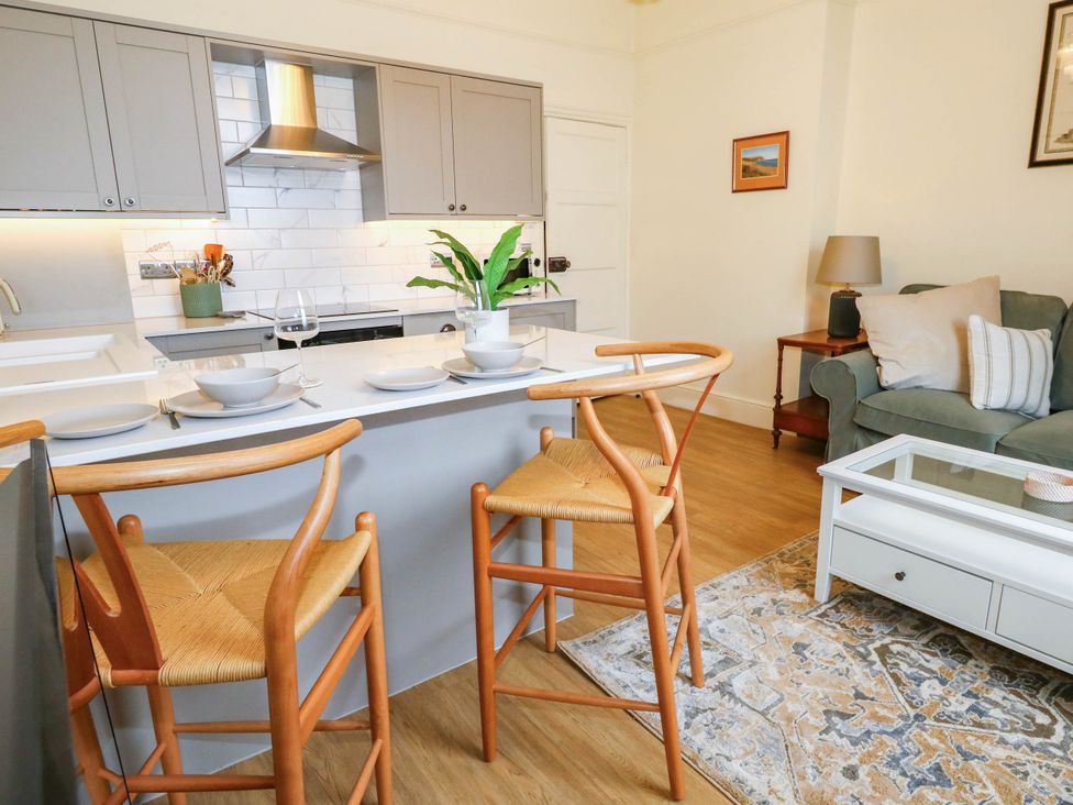 A kitchen with bar stools and a living area at 123 On The Sea - The Cubby Weymouth