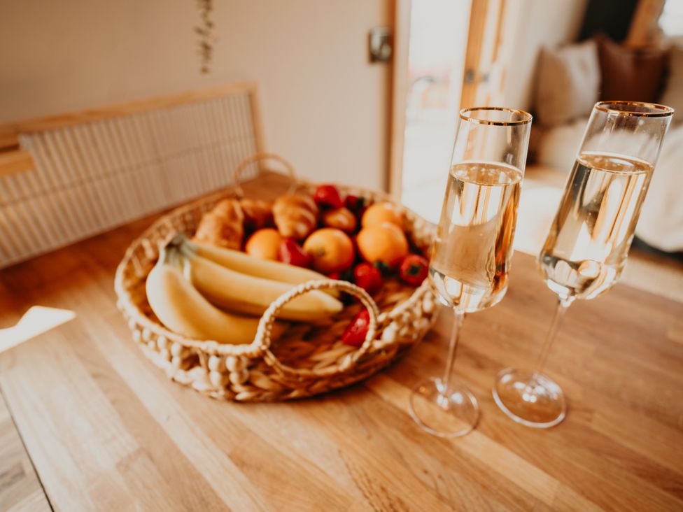 A kitchen with a basket of fruit and two glasses of sparkling wine at Driftwood in Carreglefn near Llanfechell