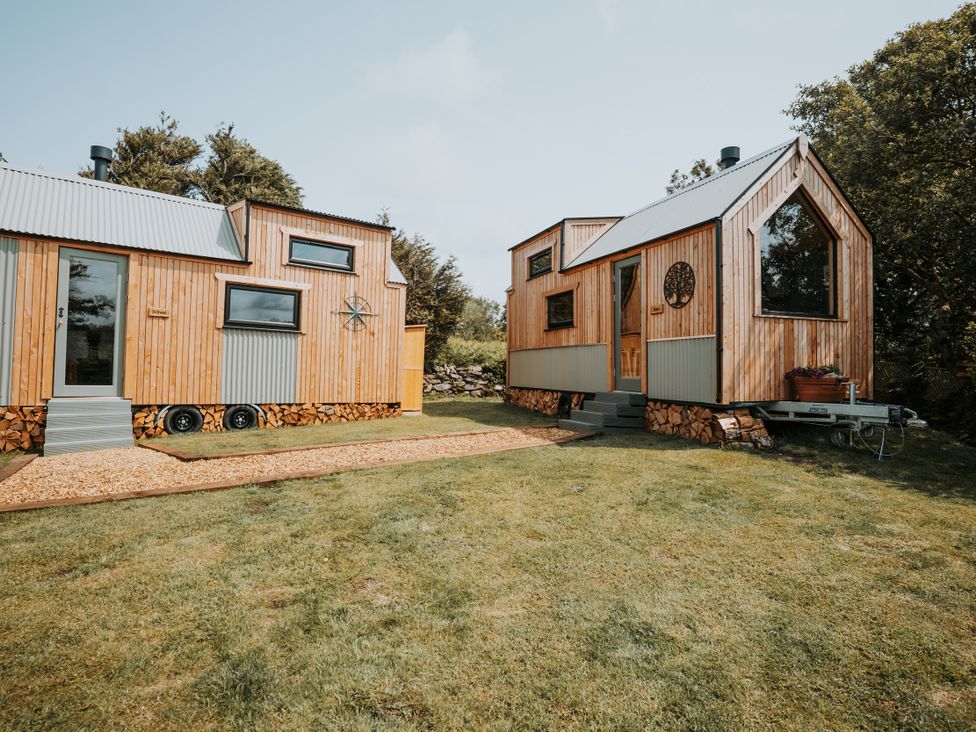 Two tiny houses with wooden exteriors and metal roofs in a garden at Rowan near Llanfechell