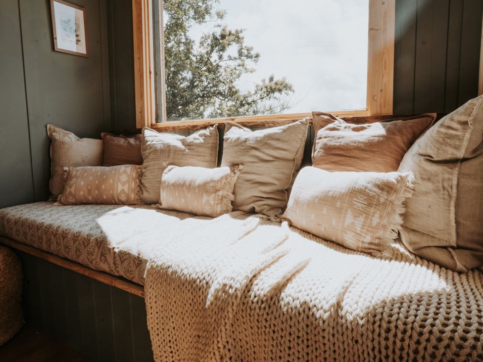 A snug with cushions and a blanket by a window at Rowan in Carreglefn near Llanfechell