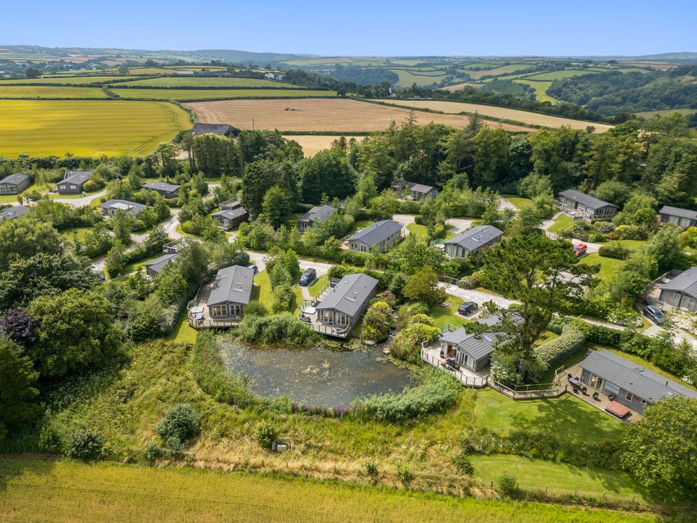 A view of holiday lodges around a pond at 3 Meadow Retreat in Dobwalls