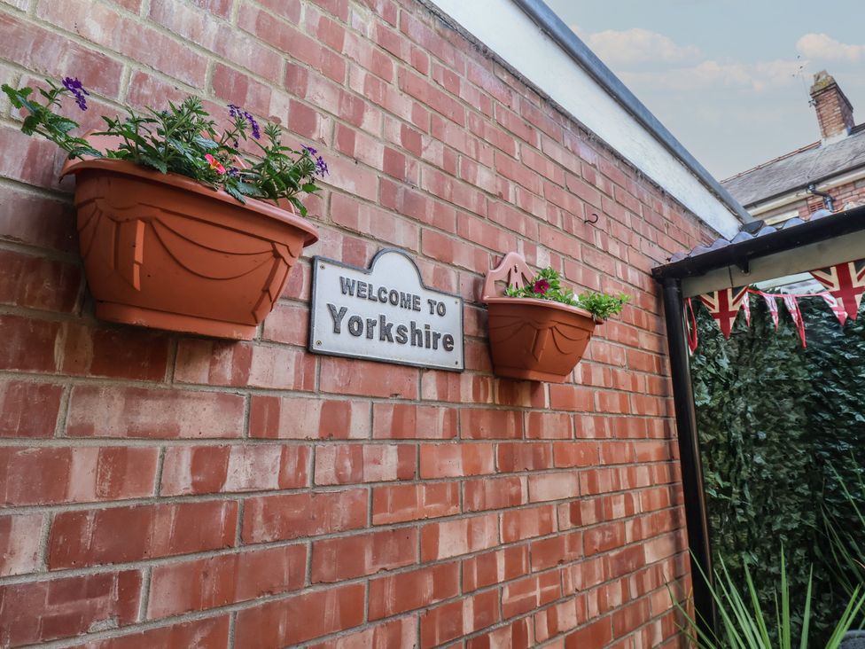 A wall with potted plants and a welcome sign at Postman’s Lodge in Great Ayton