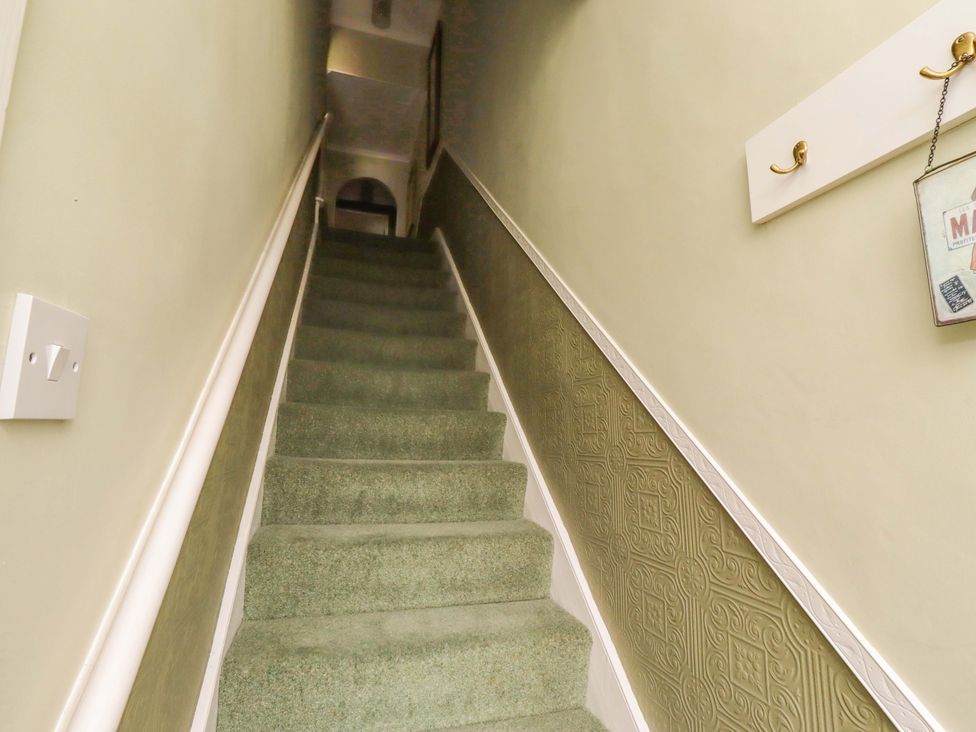 A staircase with green carpet and wall decor at Rose Briar Cottage in Morpeth