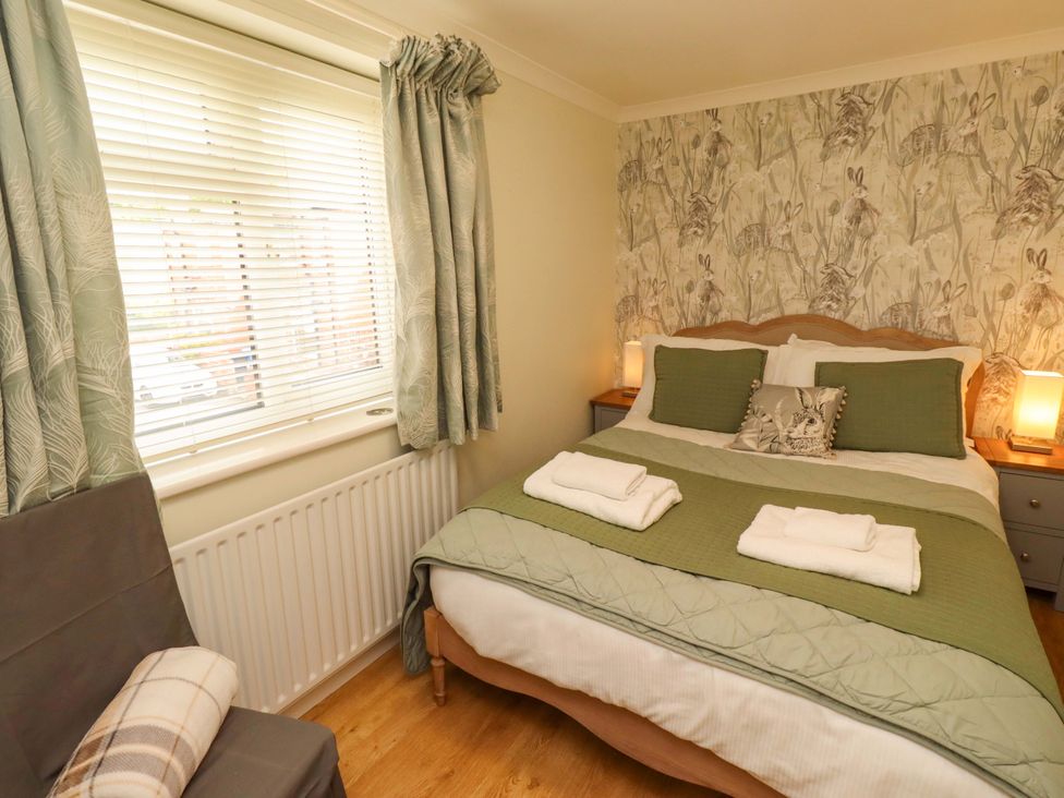 A bedroom with a bed, bedside table and window at Rose Briar Cottage in Morpeth