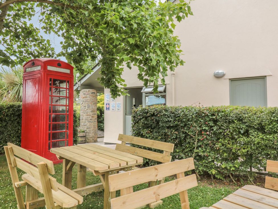 A garden with a telephone box and wooden seating at Maple Lodge Teigngrace near Kingsteignton